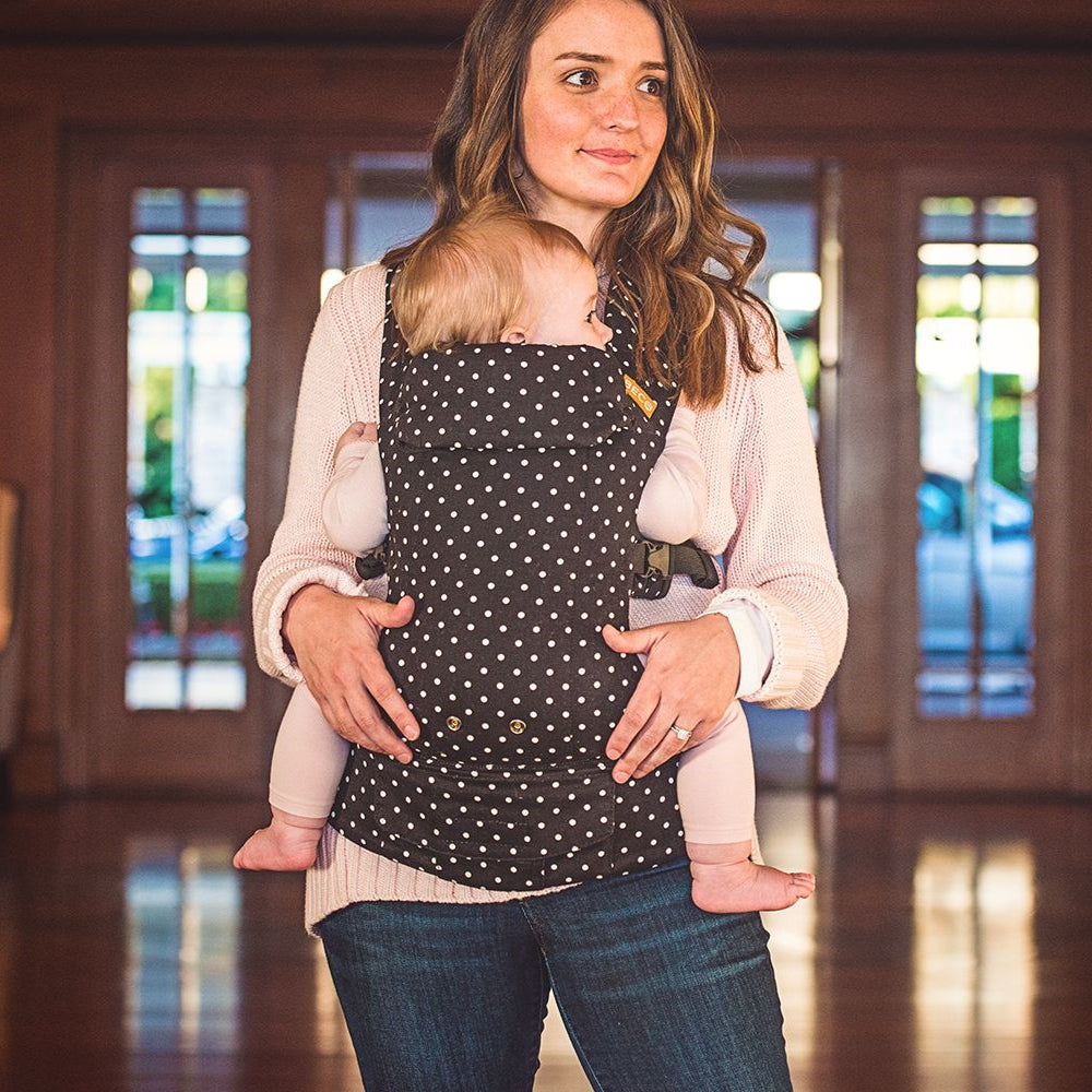 Baby in front carry facing in position in a Beco Gemini baby carrier in black with white polka dots